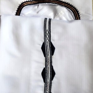 May include: White shirt with a black and white embroidered trim down the front and a black, gold, and maroon embroidered trim around the neckline.