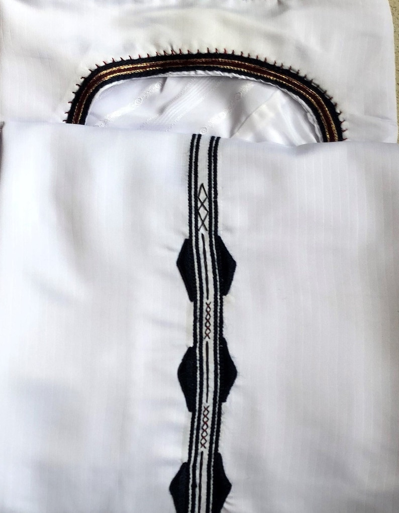 May include: White shirt with a black and white embroidered trim down the front and a black, gold, and maroon embroidered trim around the neckline.