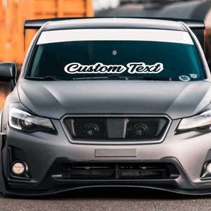 May include: A gray Subaru with a white windshield banner that says "Custom Text".