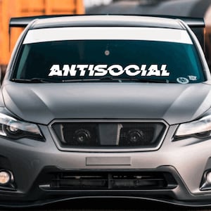 May include: A gray car with a white windshield banner that reads "ANTISOCIAL".