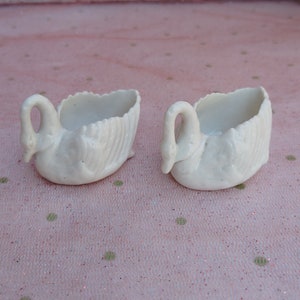 May include: Two white porcelain swan-shaped dishes. The dishes are small and have a delicate design.