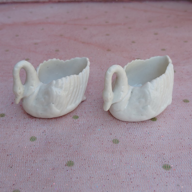 May include: Two white porcelain swan-shaped dishes. The dishes are small and have a delicate design.