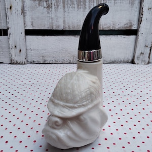 Puede incluir: Botella de cerámica blanca con forma de bulldog con un tapón negro en forma de pipa. La botella está sobre un fondo de lunares rojos y blancos.