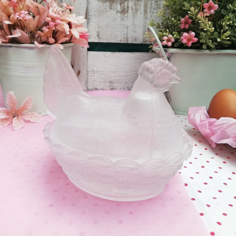 May include: A frosted glass chicken shaped dish with a nest design. The dish is white and has a textured surface.
