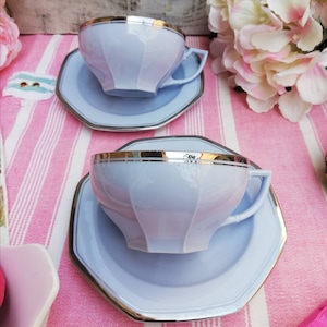 Puede incluir: Dos tazas de té azul claro con ribete dorado y platillos octogonales a juego. Las tazas y los platillos tienen un diseño delicado y femenino.