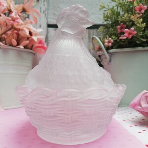 May include: A frosted glass hen-shaped sugar bowl with a basket-shaped base. The hen is white with a pink tint and has a detailed design.