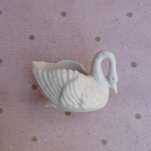 May include: White ceramic swan planter with a detailed design. The swan has a curved neck and a wide, open beak. The planter is ideal for small plants or succulents.