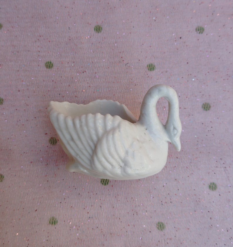 May include: White ceramic swan planter with a detailed design. The swan has a curved neck and a wide, open beak. The planter is ideal for small plants or succulents.