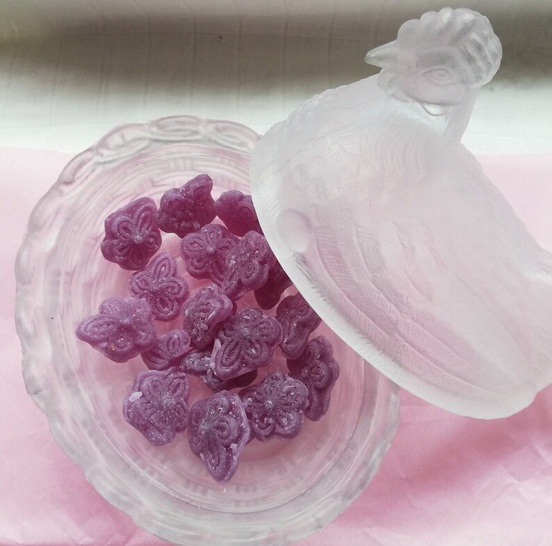 May include: A clear glass hen-shaped dish with a lid, filled with purple butterfly-shaped sweets.