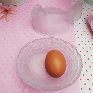 May include: A frosted glass hen-shaped egg holder with a matching nest-shaped dish. The dish contains a brown egg.