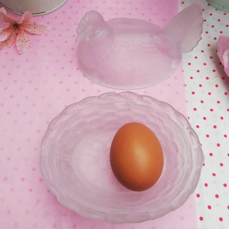 May include: A frosted glass hen-shaped egg holder with a matching nest-shaped dish. The dish contains a brown egg.