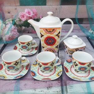 Könnte beinhalten: Ein Set aus bunten Teetassen und Untertassen mit floralem Muster. Das Set beinhaltet eine Teekanne und eine Zuckerdose, alle mit passenden Mustern. Die Teetassen sind weiß mit einem bunten floralen Muster und goldenen Akzenten.
