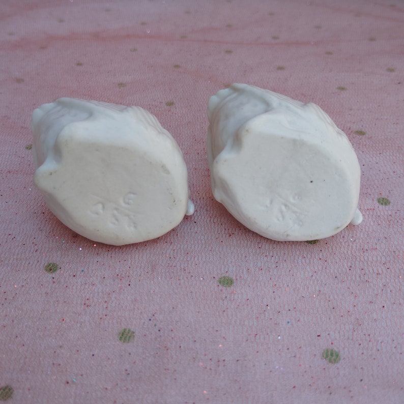May include: Two white ceramic bird figurines with a textured surface. The bottom of each figurine has the word "ANG" stamped on it.