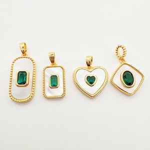 Puede incluir: Cuatro colgantes dorados con incrustaciones de nácar blanco y piedras preciosas verde esmeralda. Los colgantes tienen diferentes formas: un rectángulo, un cuadrado, un corazón y un óvalo. Cada colgante tiene una argolla dorada.
