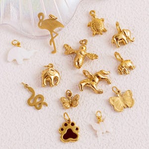 Puede incluir: Una colección de colgantes dorados con varios diseños inspirados en animales y la naturaleza. Los colgantes incluyen un flamenco, una tortuga, un elefante, una serpiente, una mariposa, una huella de pata y un caballito de mar. Los colgantes están diseñados para la fabricación de joyas.