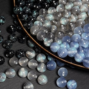 May include: A collection of iridescent glass beads in shades of blue, grey, and black. The beads are round and have a sparkly finish.