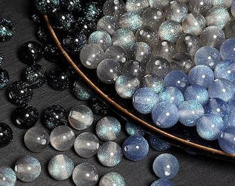 May include: A collection of iridescent glass beads in shades of blue, gray, and black. The beads are round and have a sparkly finish.