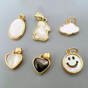 Peut inclure: Plusieurs pendentifs dorés aux formes variées. On y trouve un ovale, un lapin, un nuage, deux cœurs et un smiley. Chaque pendentif est orné d'une incrustation en nacre ou en coquillage noir.