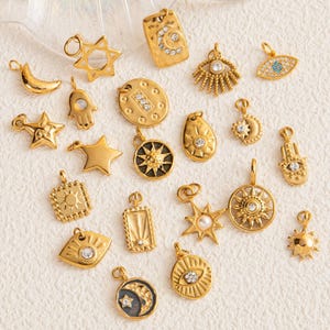 Puede incluir: Una colección de colgantes dorados de varias formas, incluyendo estrellas, lunas, soles y un ojo. Algunos colgantes presentan cristales incrustados. Los colgantes están diseñados para la fabricación de joyas o como amuletos.
