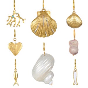 Puede incluir: Una colección de pendientes dorados con colgantes con temática oceánica. Los diseños incluyen una rama de coral con un acento turquesa, una concha con detalles de cristal, un corazón, un pez, una caracola y una perla.