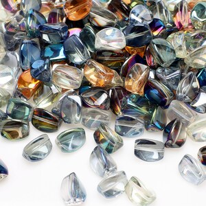 Pode incluir: Uma cole&ccedil;&atilde;o de contas de vidro iridescentes em v&aacute;rias formas e tamanhos. As contas exibem uma gama de cores, incluindo azul, &acirc;mbar e transparente, com uma qualidade brilhante e reflexiva. As contas est&atilde;o espalhadas, criando uma exibi&ccedil;&atilde;o texturizada e visualmente atraente.
