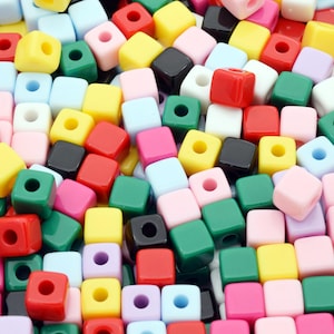 Puede incluir: Un gran surtido de cuentas de plástico cúbicas de colores. Las cuentas son de varios colores, incluyendo rojo, verde, azul, amarillo, rosa, negro y blanco.