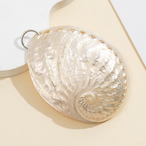 Pode incluir: Um pingente ovalado perolado com uma argola prateada. A concha iridescente apresenta um desenho em espiral e pequenos pontos castanhos na borda. A superf&iacute;cie da concha tem uma textura natural. Forma natural e org&acirc;nica.