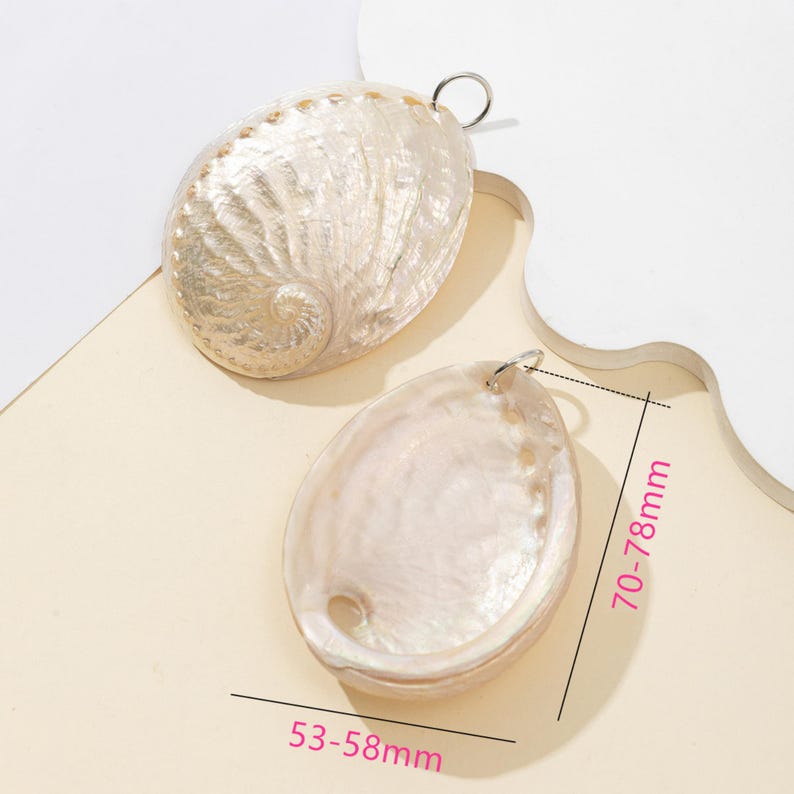 Pode incluir: Dois pingentes ovais iridescentes de concha de abalone com argolas prateadas. Medem 5,3-5,8 cm de largura e 7-7,8 cm de comprimento. As conchas t&ecirc;m um brilho perolado com padr&otilde;es naturais, ideais para joias ou artesanato.
