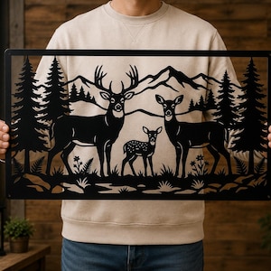 May include: A rectangular black metal wall art piece featuring a laser-cut silhouette of a deer family consisting of a buck, a doe, and a fawn standing in a forest landscape with pine trees, ferns, and mountain peaks in the background.