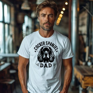 May include: White t-shirt with a black and white illustration of a Cocker Spaniel dog. The text "Cocker Spaniel Dad" is printed on the shirt.