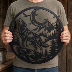 May include: A circular black metal wall art piece featuring a cutout design of a wolf howling at a crescent moon. The scene includes silhouettes of jagged mountain peaks, a dense pine forest, and several birds flying in the night sky.