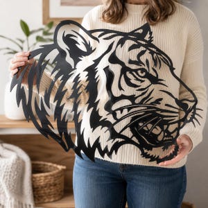 May include: A black metal wall art piece shaped like the head of a tiger in profile. The design features intricate cutouts that define the tiger's facial features, ears, and striped fur pattern, creating a bold silhouette with sharp, jagged edges.