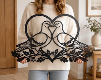May include: A black metal wall art piece featuring a silhouette of two doves facing each other within a heart-shaped outline. The birds are perched on a branch with detailed oak leaves at the base, creating a symmetrical and decorative design.
