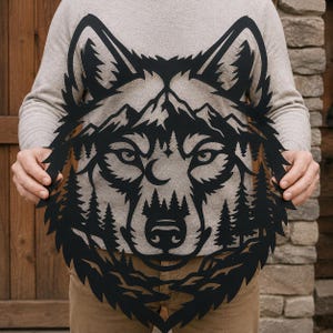 May include: A black metal wall art piece featuring a detailed cutout of a wolf head. The design incorporates a mountain range across the forehead and a dense forest of pine trees filling the lower portion of the face, with a small crescent moon.