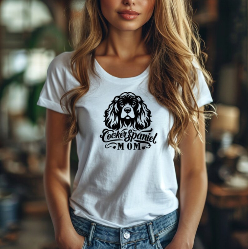 May include: White t-shirt with a black and white illustration of a Cocker Spaniel dog and the text "Cocker Spaniel MOM".