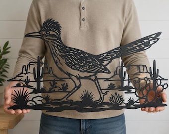 Puede incluir: Una pieza de arte mural de metal negro con la silueta detallada de un correcaminos caminando por un paisaje desértico. El diseño incluye recortes de cactus saguaro, chumberas y mesas distantes sobre una línea de horizonte plana.