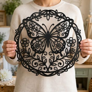 May include: A circular black wall art piece featuring a detailed laser-cut butterfly at the centre, surrounded by an intricate floral and vine pattern within a decorative border. The design is symmetrical, showcasing delicate cutouts throughout.