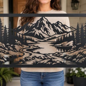 Peut inclure: Une pièce d'art mural rectangulaire en métal noir présentant un design de paysage découpé au laser. La scène représente une chaîne de montagnes en arrière-plan, un lac calme au centre et une forêt dense de pins des deux côtés avec un terrain rocheux.