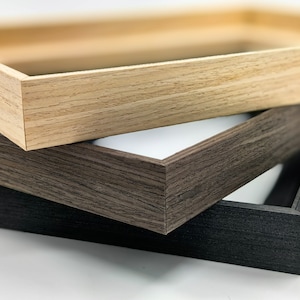 Puede incluir: Primer plano de tres marcos de fotos de madera en diferentes colores: marrón claro, marrón oscuro y negro. Los marcos están apilados, mostrando sus esquinas y el espacio blanco en el interior. La veta de la madera es visible.