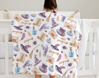 May include: A white baby blanket with a whimsical witch theme. The blanket features a repeating pattern of witch hats, broomsticks, potion bottles, stars, feathers, and scrolls with the name "Trinity" written on them.