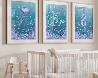 May include: Three framed watercolor art prints with an ocean theme. The prints feature a jellyfish, a seahorse, and the name "Eloise" with an initial. The artwork has a teal background with purple and pink coral and fish.