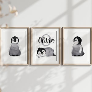 May include: Three framed prints featuring black and white illustrations of penguins. The middle print has the name "Olivia" written in black with a gray circle around the letter "O".