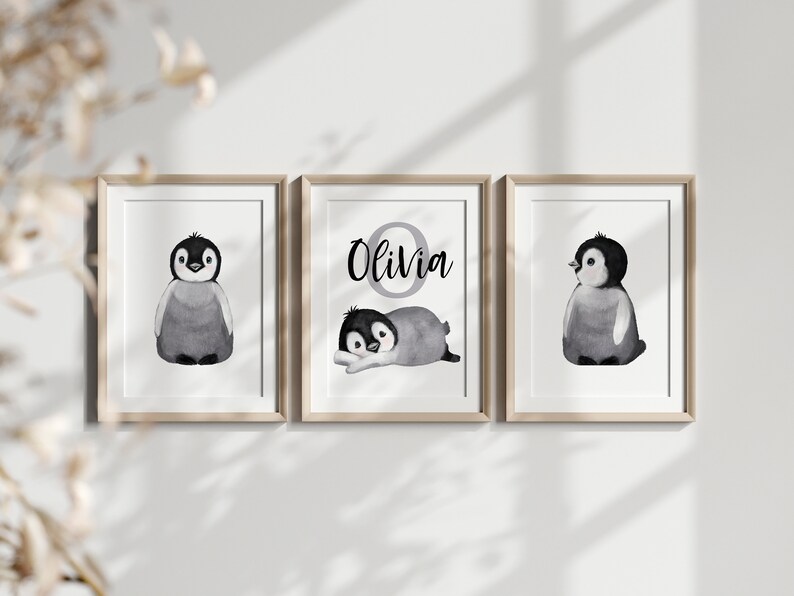 May include: Three framed prints featuring black and white illustrations of penguins. The middle print has the name "Olivia" written in black with a gray circle around the letter "O".