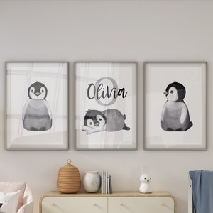 May include: Three framed watercolor prints featuring black and white penguin illustrations. The middle print has the name "Olivia" written in black cursive lettering.