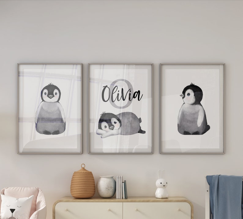 May include: Three framed watercolor prints featuring black and white penguin illustrations. The middle print has the name "Olivia" written in black cursive lettering.
