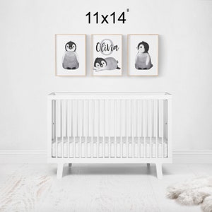 May include: Three framed prints with watercolor penguin illustrations. The center print features the name "Olivia" in a circle with a penguin inside. The prints are 11x14 inches and are displayed above a white crib.
