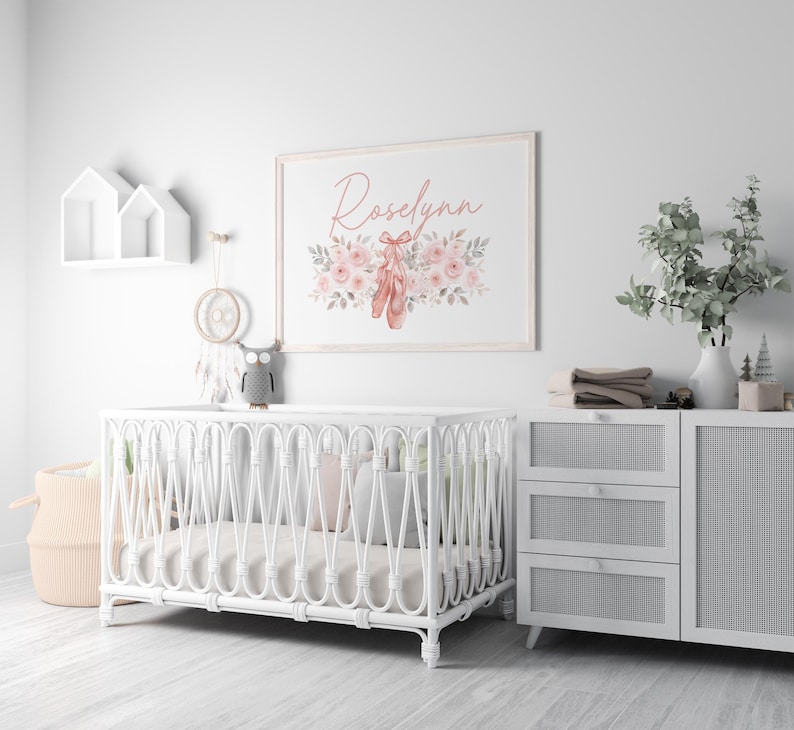 May include: A nursery scene with a white crib, a framed print with the name "Roselynn" and ballet shoes, and a white dresser. The print features pink flowers and ballet shoes. A decorative owl sits on the crib.