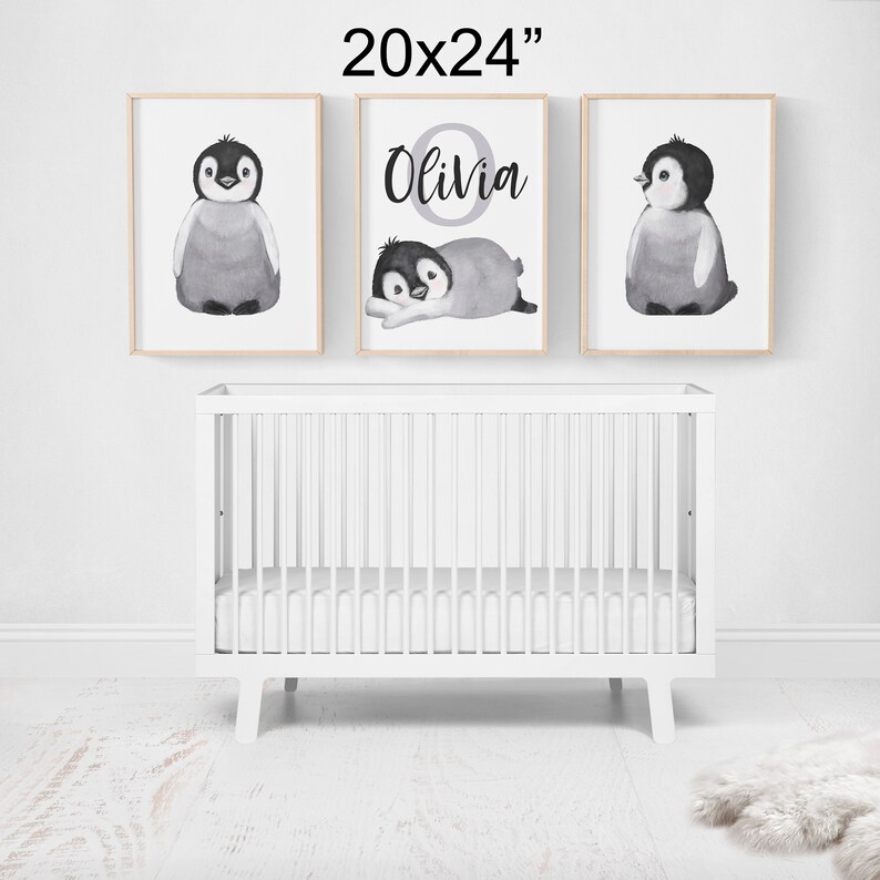 May include: Three black and white watercolor penguin illustrations in 20x24 inch frames. The center frame features the name "Olivia" in a gray circle. The frames are hung on a white wall above a white crib.