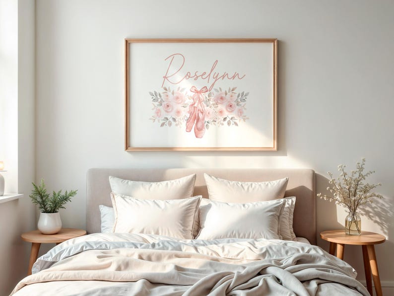 May include: A framed print with the name "Roselynn" in cursive script, surrounded by pink flowers, leaves, and ballet shoes. The artwork is displayed above a bed with white bedding and pillows. The frame is made of wood.