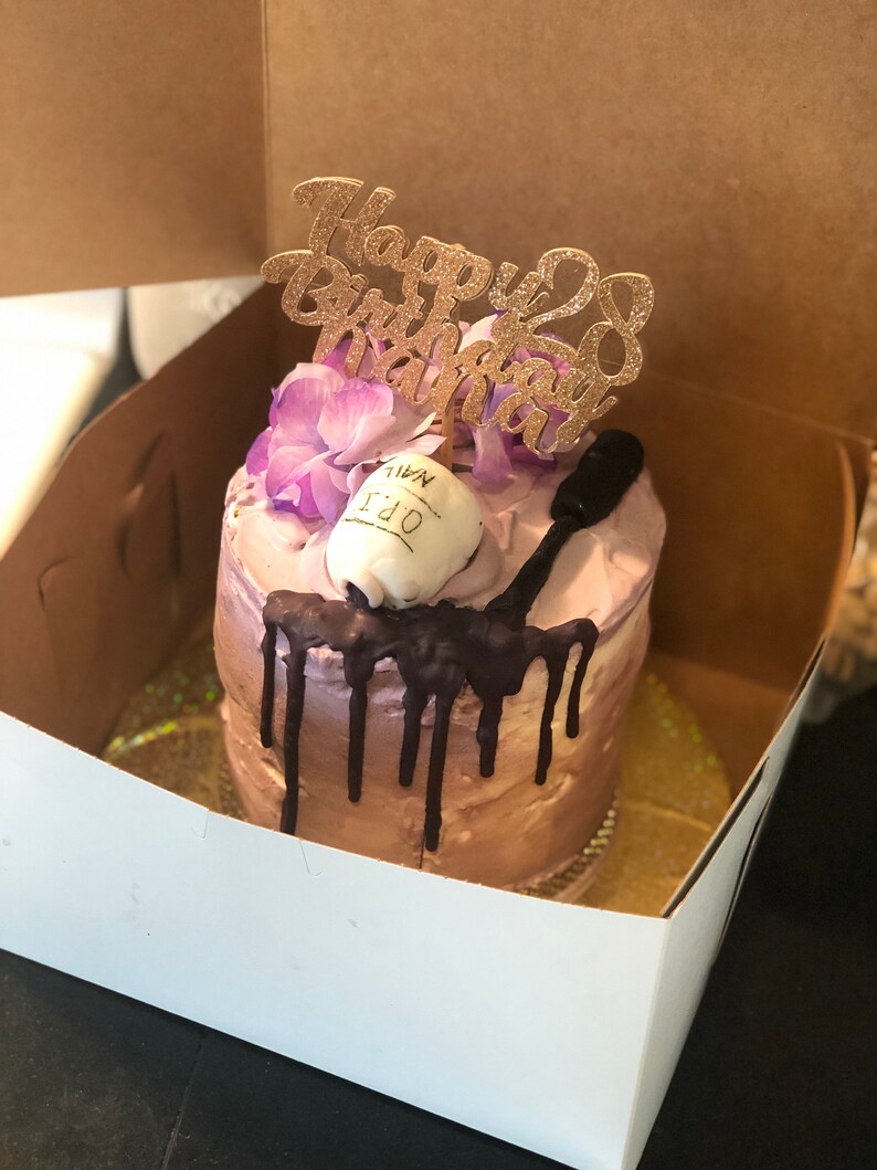 K&ouml;nnte beinhalten: Ein kleiner, einstufiger Kuchen, der mit lila Blumen, einem Schokoladen&uuml;berzug und einem "Happy 28th Birthday"-Topper verziert ist. Der Kuchen befindet sich in einer wei&szlig;en Schachtel.